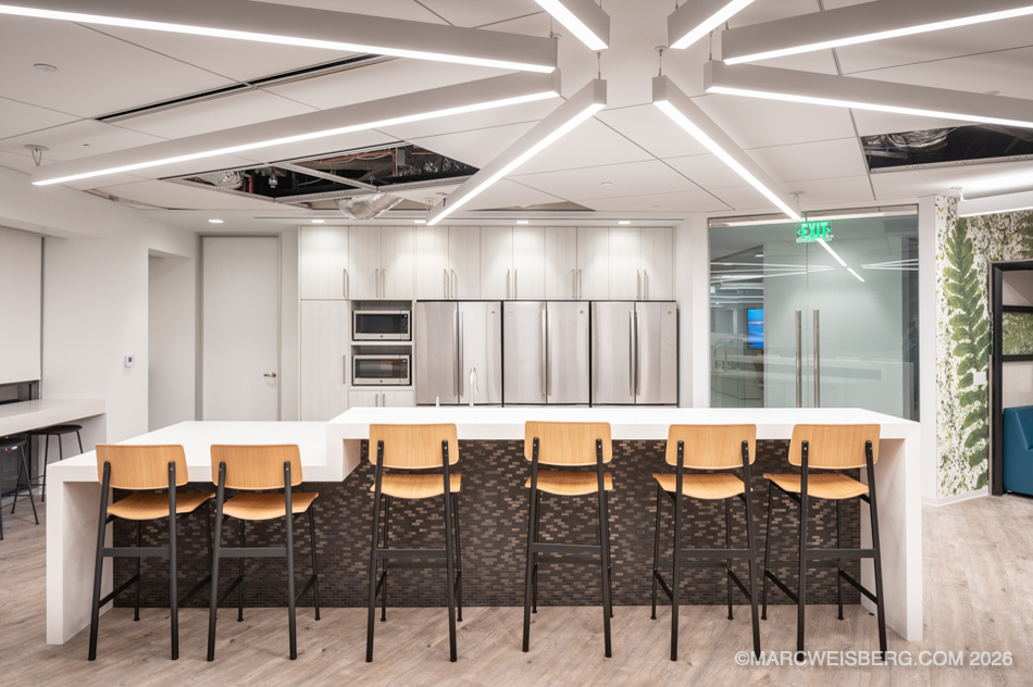 Tech office kitchen with long white island and wood bar stools